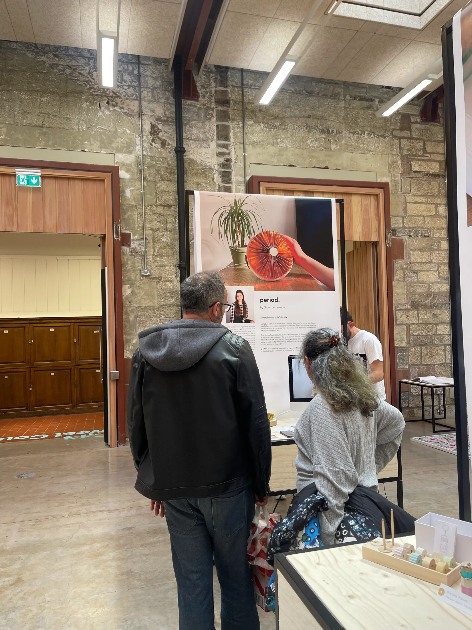 Two visitors viewing the period. poster and prototypes at the stand