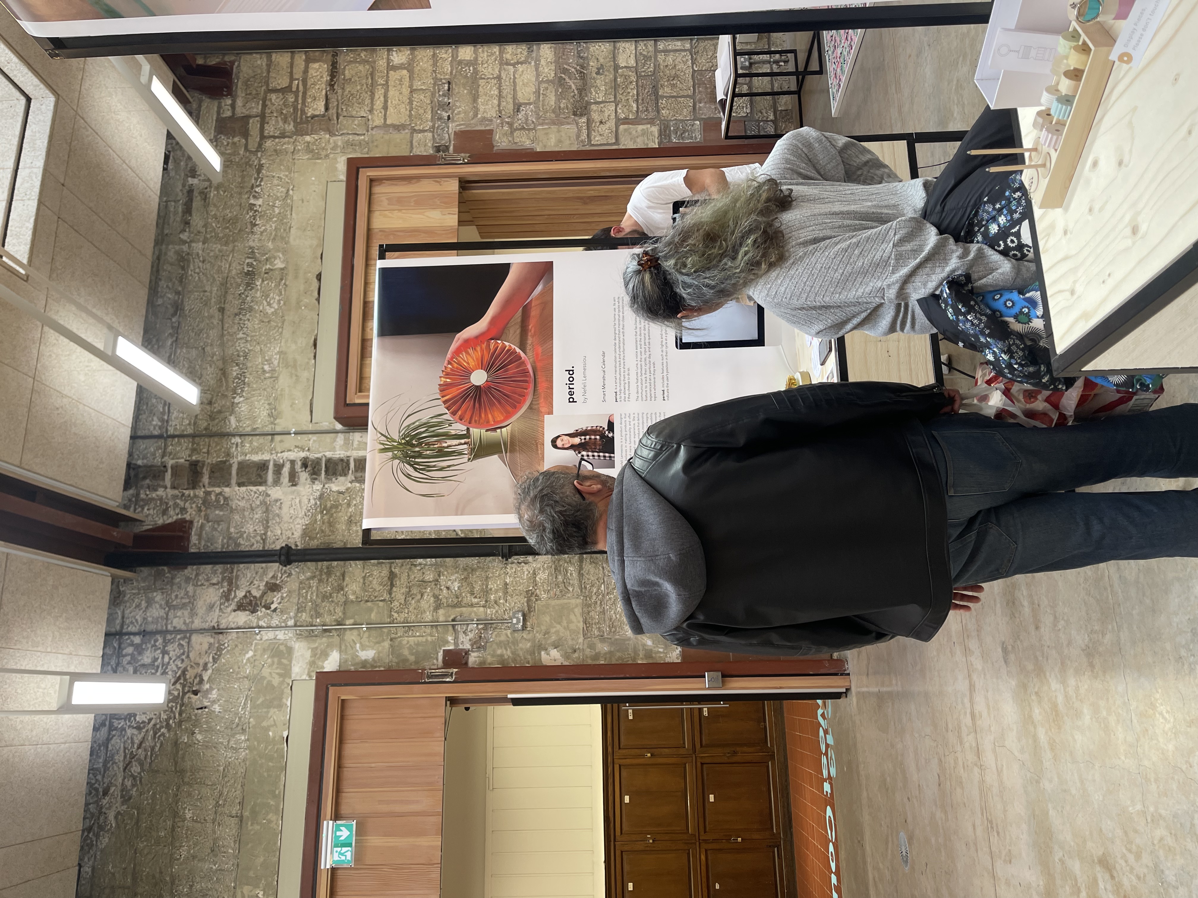 Two visitors viewing the period. poster and prototypes at the stand