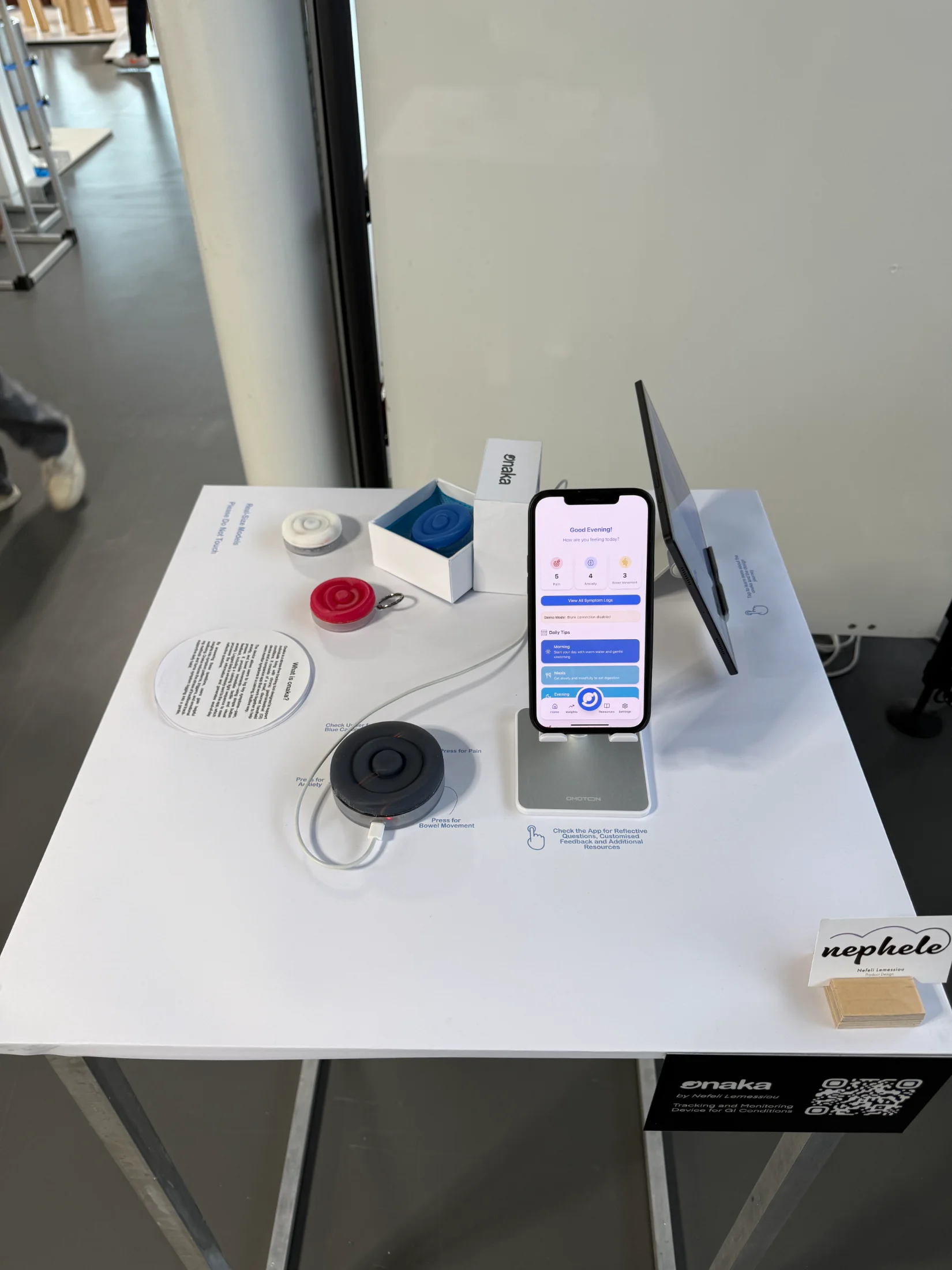 The Onaka stand at the RCA Graduation Show: real-size silicone device models and the companion app running on a phone, on a white plinth