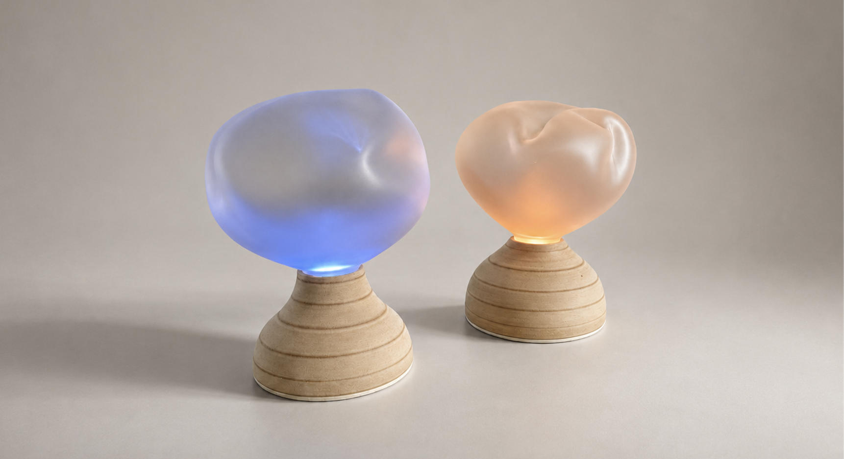 The Ilia pair, two turned-wood bases with sandblasted glass cloud diffusers, one glowing blue and one glowing warm orange