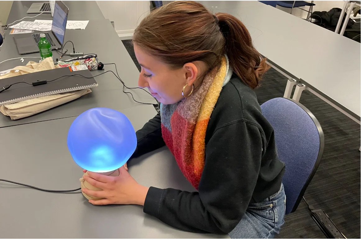 A student trying the Ilia lamp during a quick studio session, hands on the wooden base