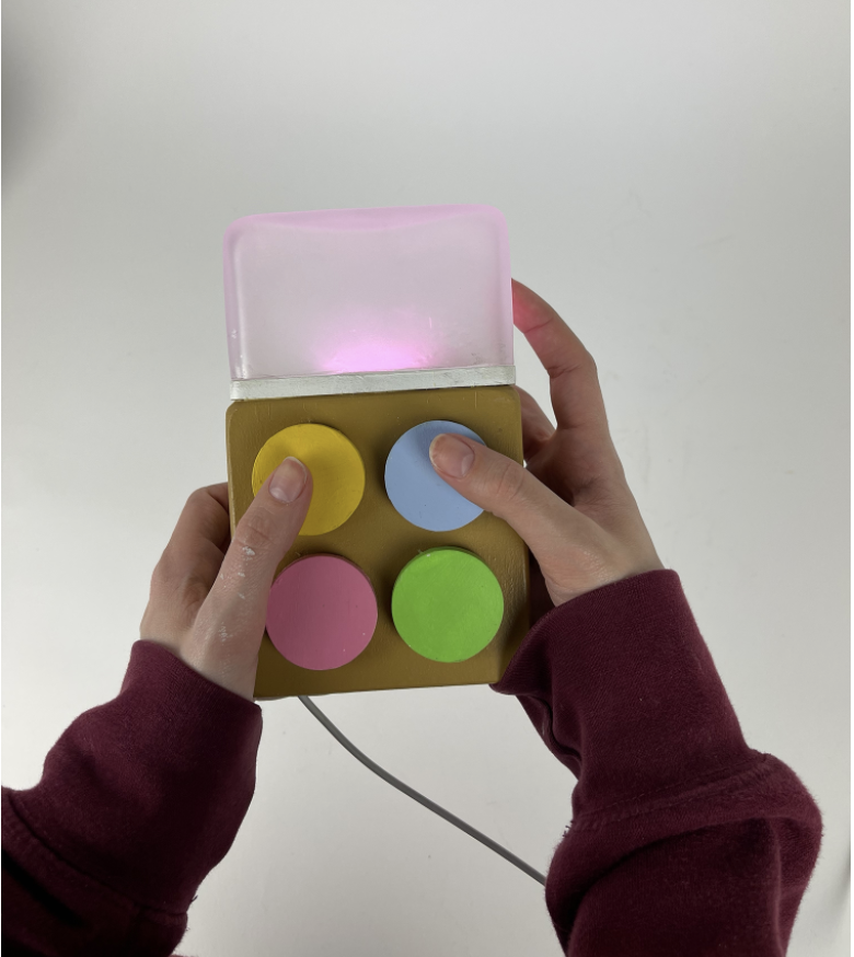 A single Milo unit held in one hand, thumb on a pastel button
