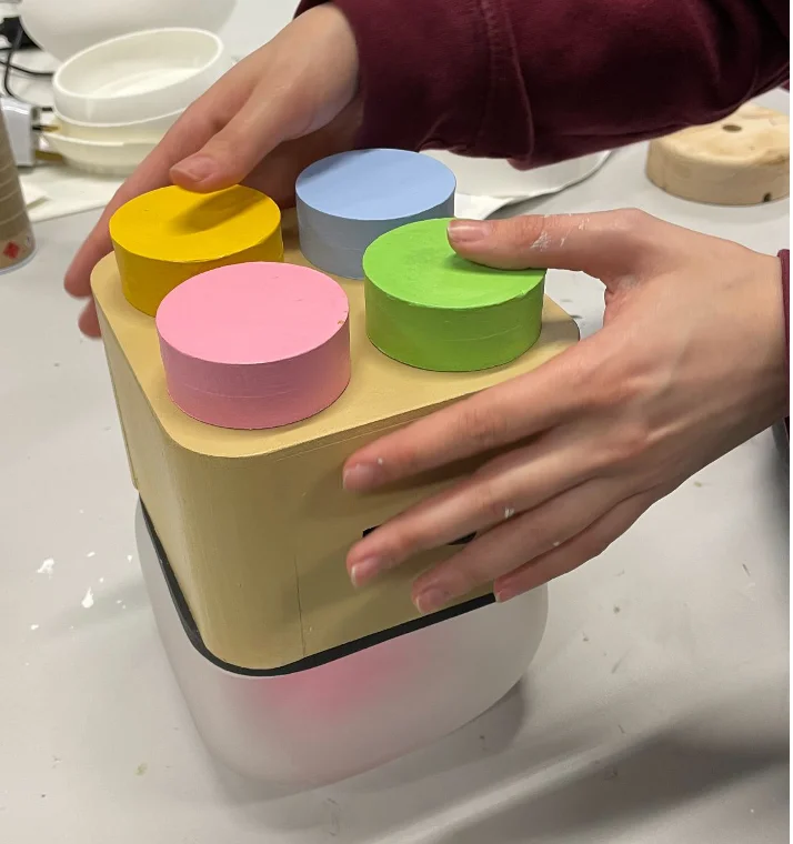 The fixed Milo prototype: a larger, almost-complete enclosure with the four pastel buttons on its top surface, sitting on a desk