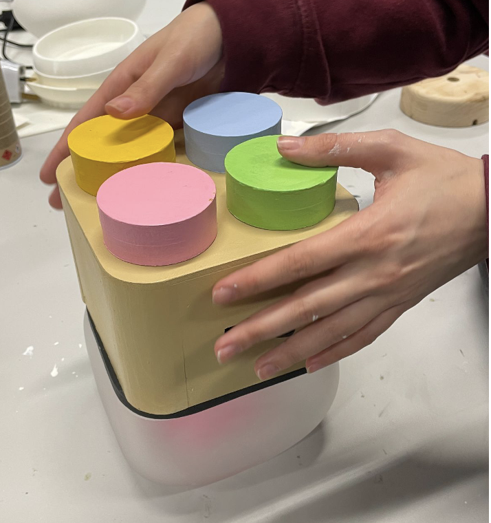 The fixed Milo prototype: a larger, almost-complete enclosure with the four pastel buttons on its top surface, sitting on a desk
