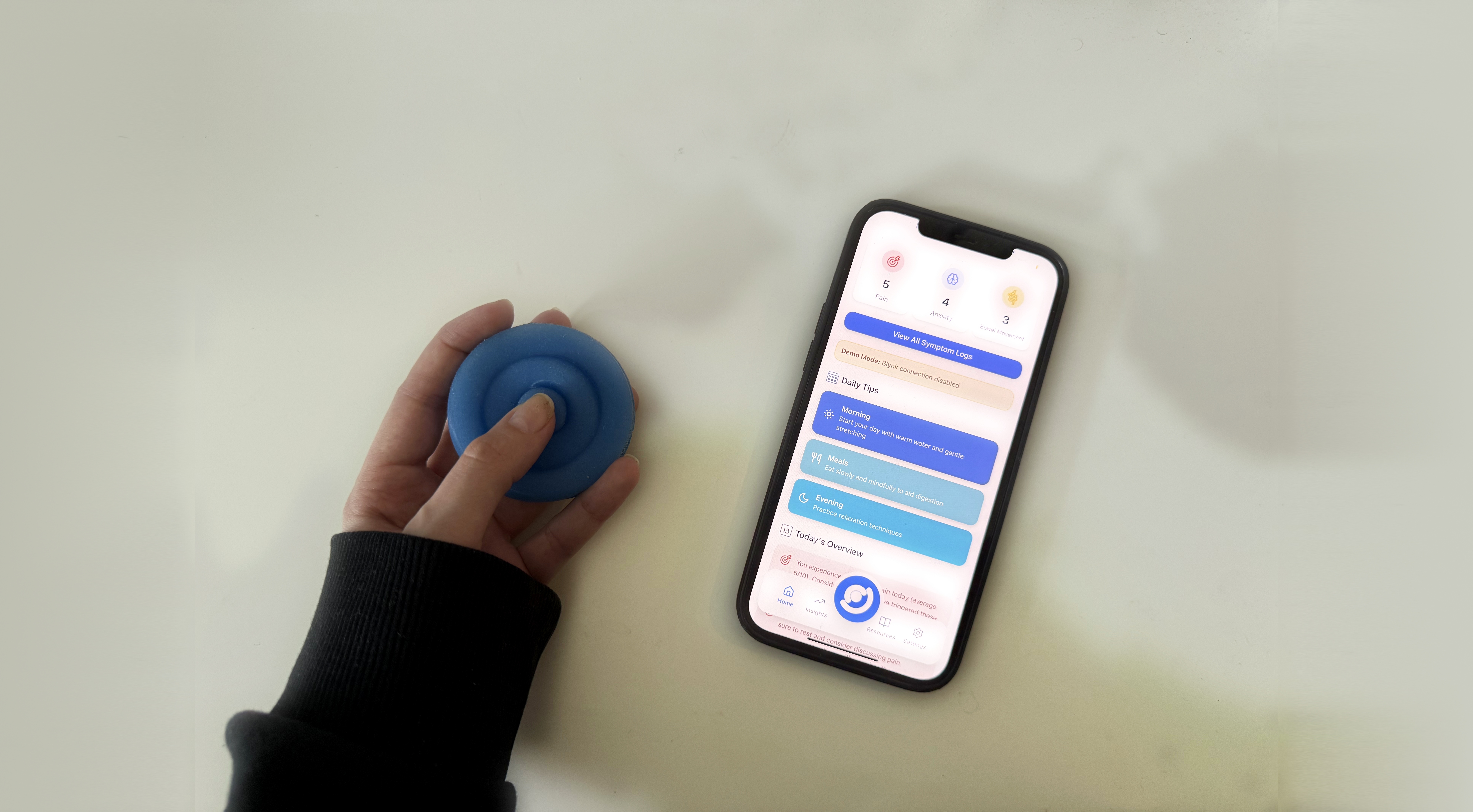 A hand pressing the blue Onaka device beside a phone showing the onaka companion app dashboard with symptom counts and daily tips