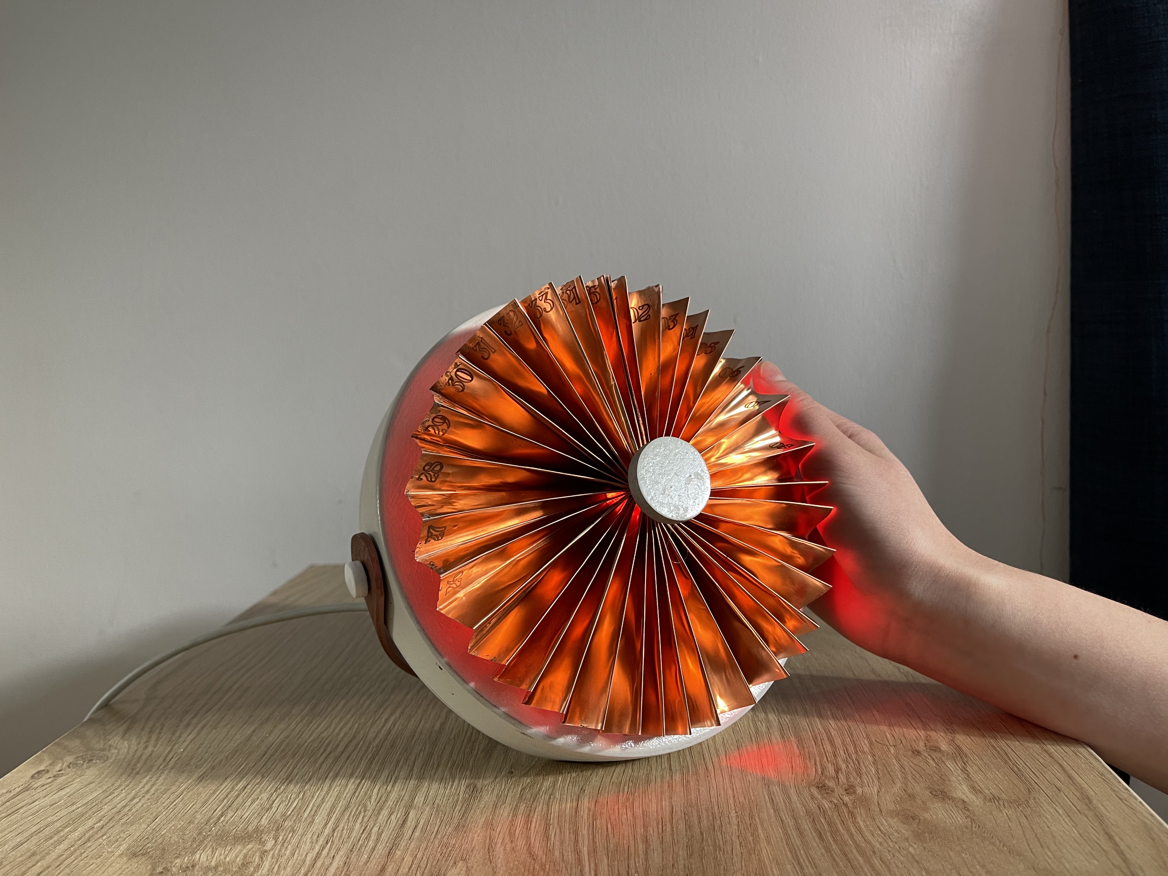 Side view of the copper device on a wooden bedside table with a hand resting on its right edge, glowing red