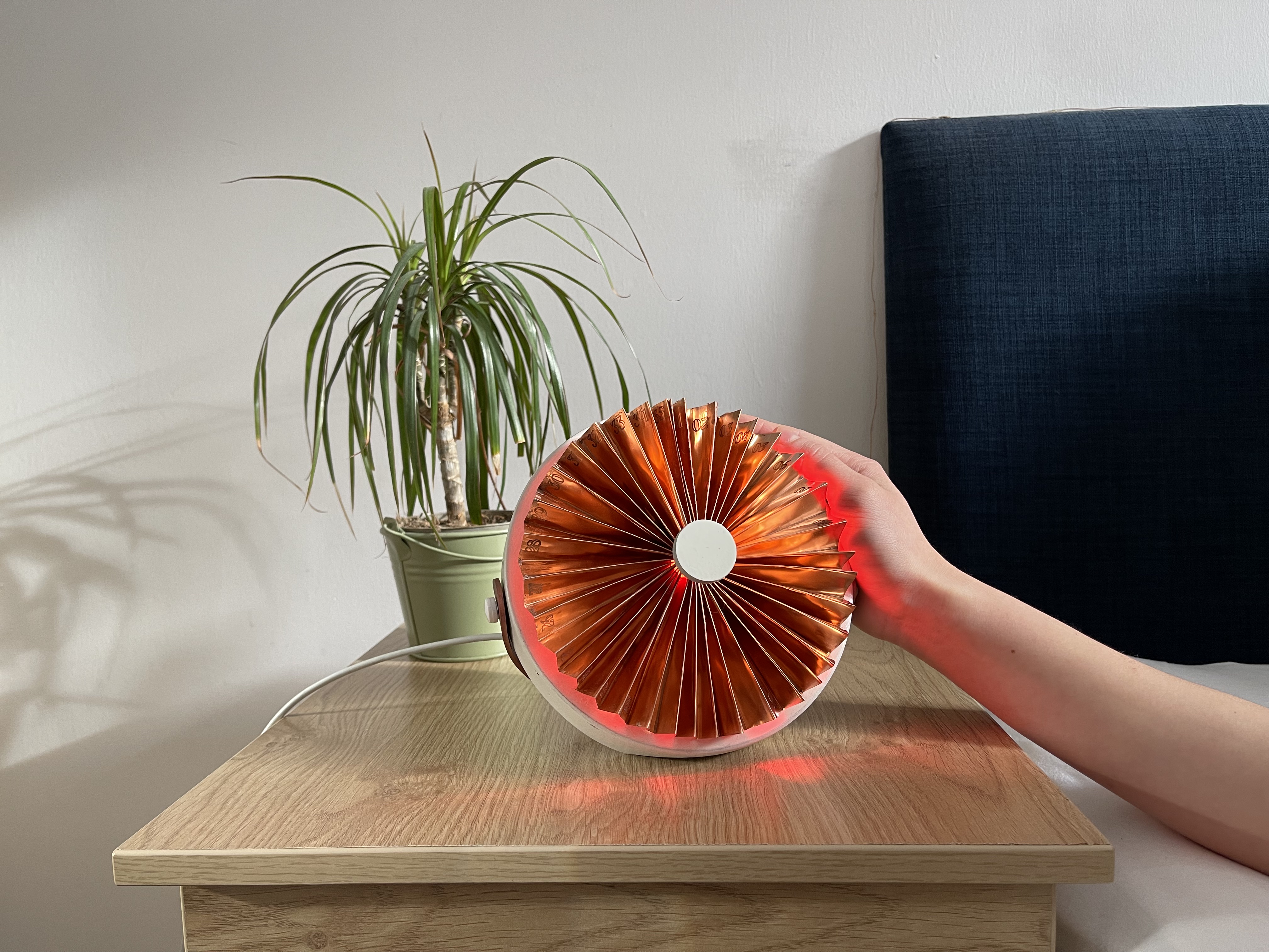 The period. device, a copper fan-shaped calendar glowing red on a bedside table