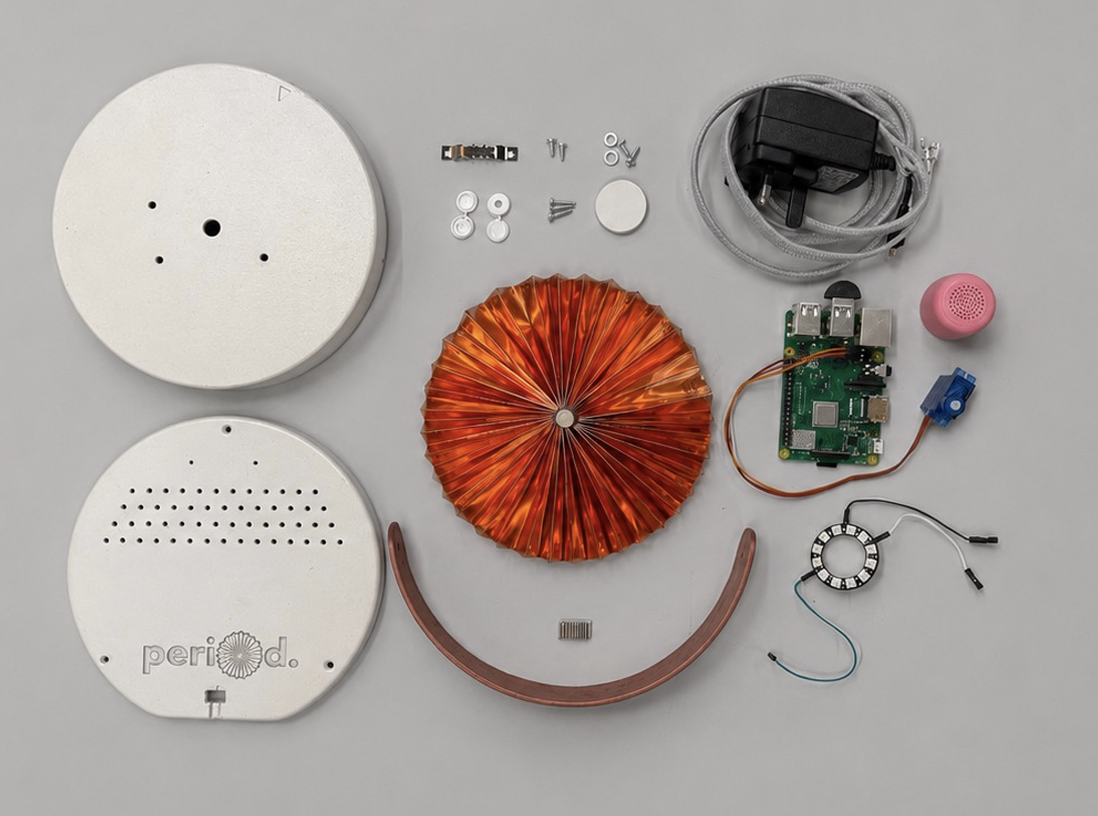Flat lay of every component used to build the period. device: base, lid, copper fan, handle, Raspberry Pi, NeoPixel ring, servo, speaker, power adapter, and screws